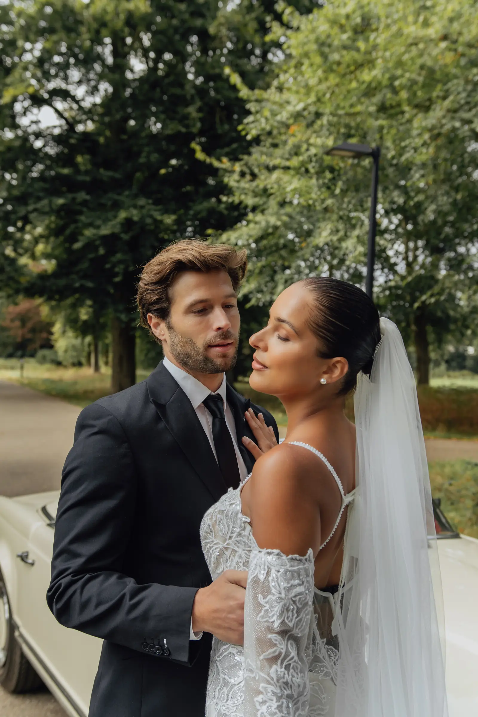 Bruid kijkt liefdevol naar haar partner bij de oldtimer