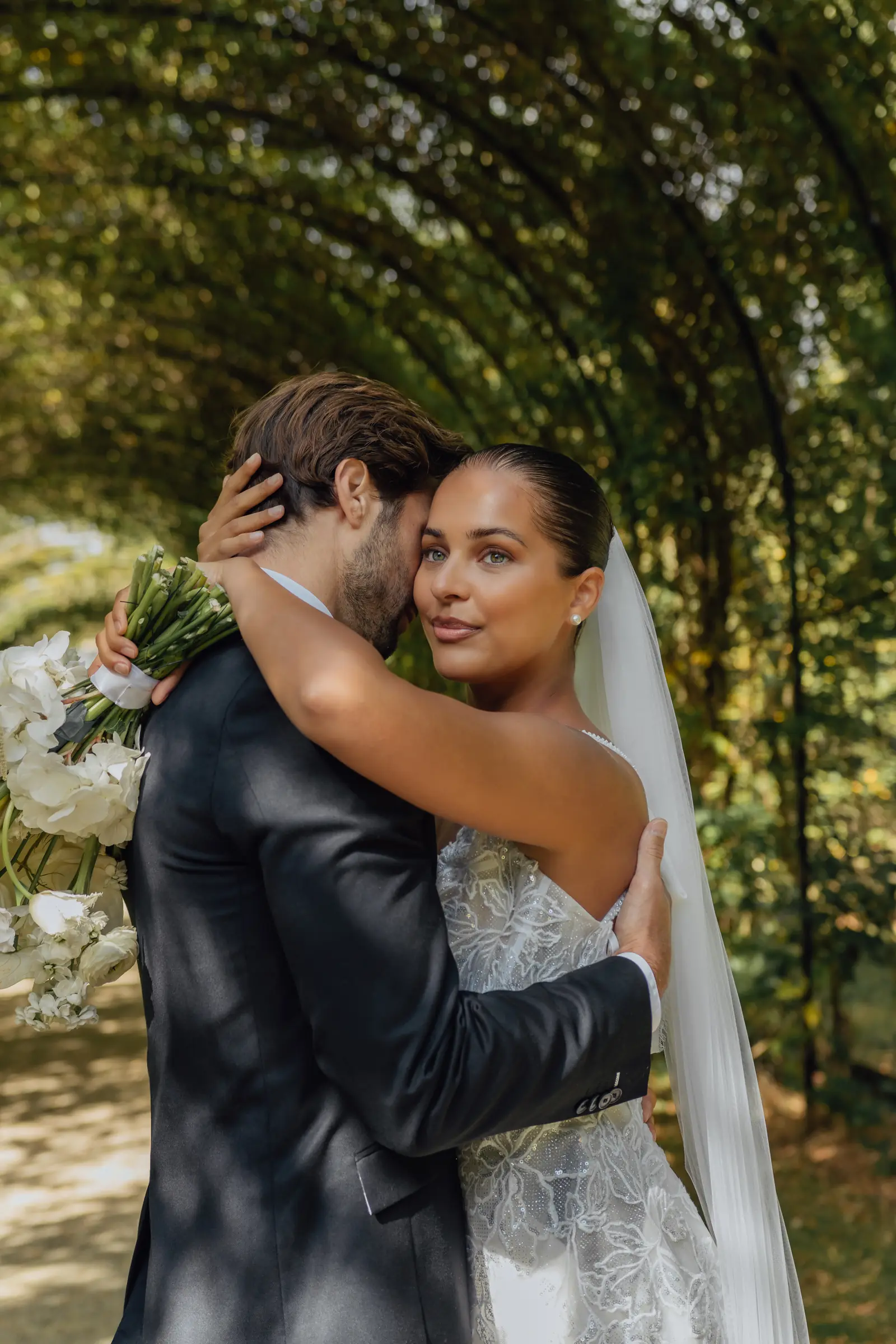 Bruid kijkt in de lens terwijl ze haar partner omhelst